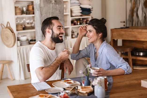 Moderna pareja morena hombre y mujer desayunando juntos mientras están sentados a la mesa en casa
