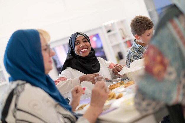 moderne afroamerikanische muslimische frau, die zusammen mit einer multiethnischen familie während eines ramadan-festes zu hause ein iftar-abendessen genießt
