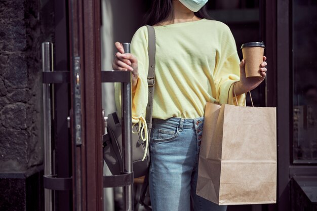 Moderne Frau in medizinischer Maske, die Bestellung beim Verlassen des Cafés hält