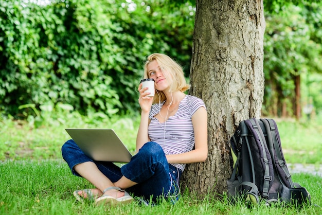 Moderne Frau mit Computer im Freien Hübsche Frau trinkt Kaffee zum Mitnehmen Sommer online Morgendiagramm Mädchen arbeiten am Laptop Mädchen trinken Kaffee zum Mitnehmen Entspannen Sie sich im Park Unter Verwendung moderner Technologien