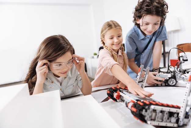 Moderne Geräte testen. Inspirierte fröhliche fröhliche Kinder, die in der Schule sitzen und mit Cyber-Robotern spielen, während sie Wissenschaftsunterricht haben