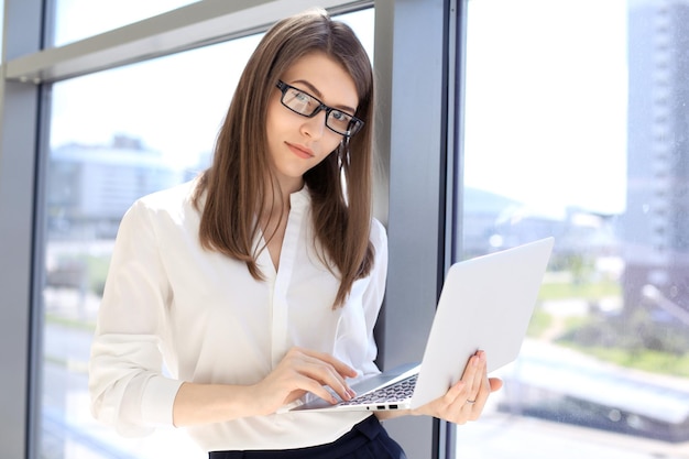 Moderne Geschäftsfrau, die auf Laptop-Computer tippt, während sie im Büro steht, bevor sie sich trifft oder präsentiert