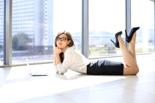 Moderne Geschäftsfrau, die mit Laptop-Computer arbeitet, während sie im Bürokopierraum auf dem Boden liegt