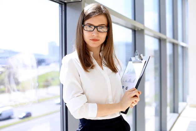 Moderne Geschäftsfrau steht und hält Papiere im Büro mit Kopierbereich