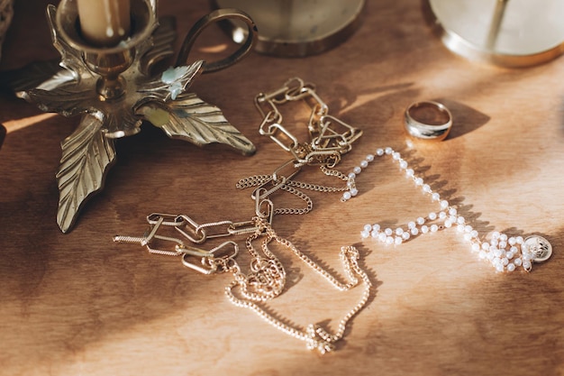 Moderne Gold- und Perlenaccessoires auf dem Tisch mit Vintage-Kerzenhaltern Halskette und Ring im Sonnenschein