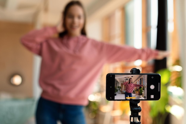 Moderne Influencerin im Teenageralter, die Videos auf dem Smartphone aufzeichnet und zu Hause vor der Kamera tanzt, selektiver Fokus