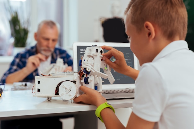 Moderne Innovationen. Netter süßer Junge, der vor dem Computer sitzt, während er mit einem Roboter spielt