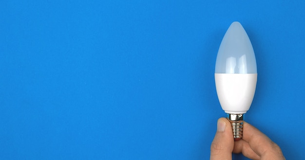 Moderne Öko-LED-Glühbirne in der Hand, blauer Hintergrund. Banner, flache Lage, Draufsicht, Platzfoto kopieren