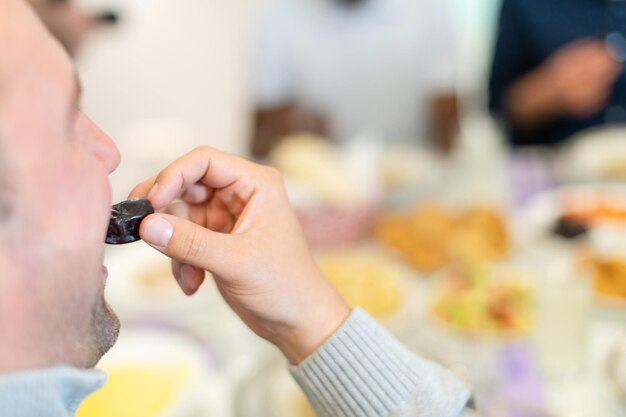 moderne multiethnische muslimische familie, die sich eine schüssel mit datteln teilt, während sie während eines ramadan-fests zu hause gemeinsam ein iftar-abendessen genießen