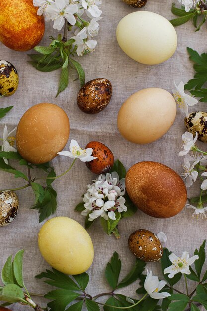 Moderne Ostereier mit Frühlingsblumen liegen flach auf rustikalem Leinenstoff Frohe Ostern Ästhetik