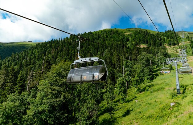 Moderne Seilbahn- oder Seilbahnkabinen mit Menschen vor grünem Tal, blauem Himmel und Berggipfeln