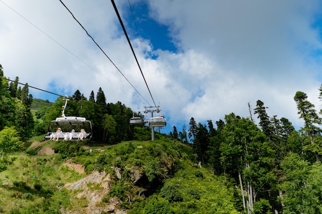 Moderne Seilbahn- oder Seilbahnkabinen mit Menschen vor grünem Tal, blauem Himmel und Berggipfeln