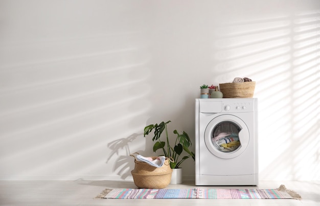 Moderne Waschmaschine und Weidenkorb mit Wäsche in der Nähe von weißer Wandfläche für Text Innenarchitektur