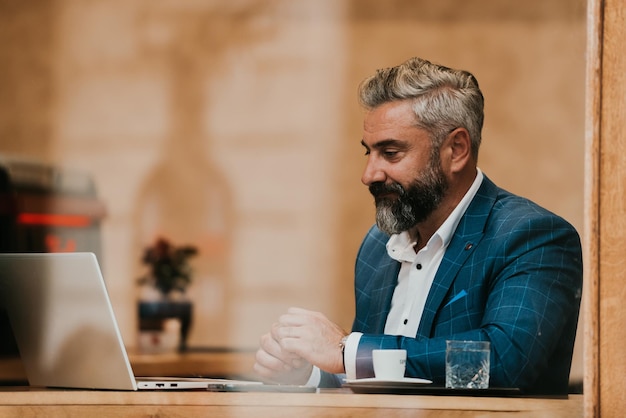 Moderner älterer Geschäftsmann, der im Café sitzt und Laptop und Smartphone verwendet