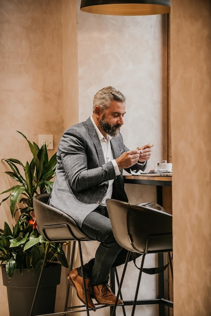 Moderner älterer Geschäftsmann raucht eine Zigarette, während er sich nach einem harten Arbeitstag in einem Café ausruht