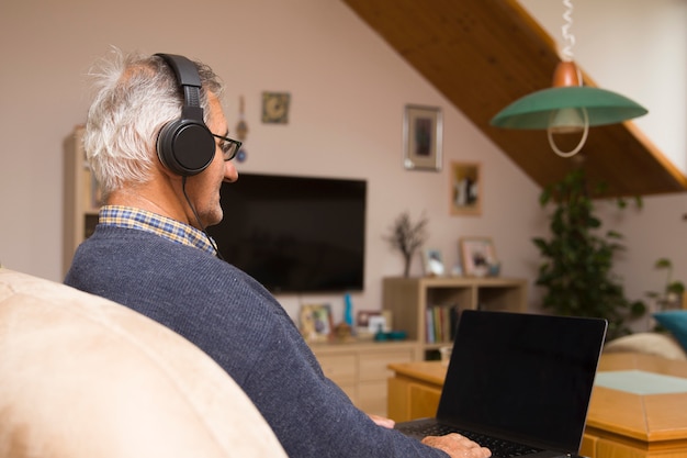 Moderner älterer Mann, der zu Hause mit Kopfhörern sitzt und Online-Videoanruf hat
