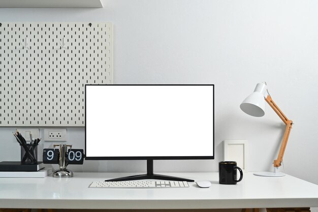 Moderner Arbeitsplatz mit einem leeren Computermonitor, einer Kaffeekuppenlampe und einem Pfahlbrett an der Wand