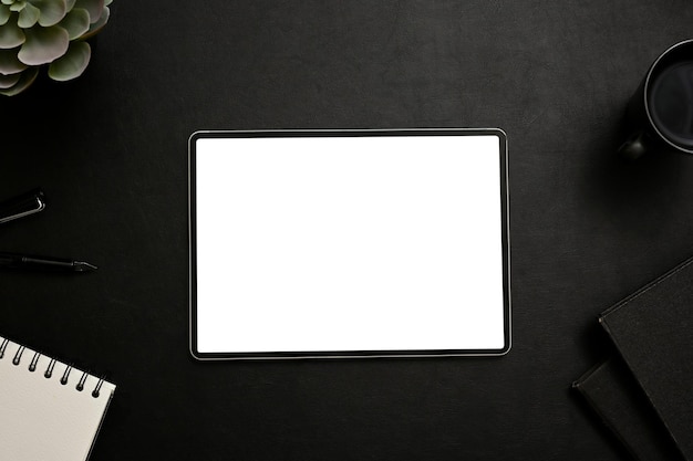 Moderner Arbeitsplatz mit Tablet-Attrappe, umgeben von Zubehör auf schwarzem Hintergrund