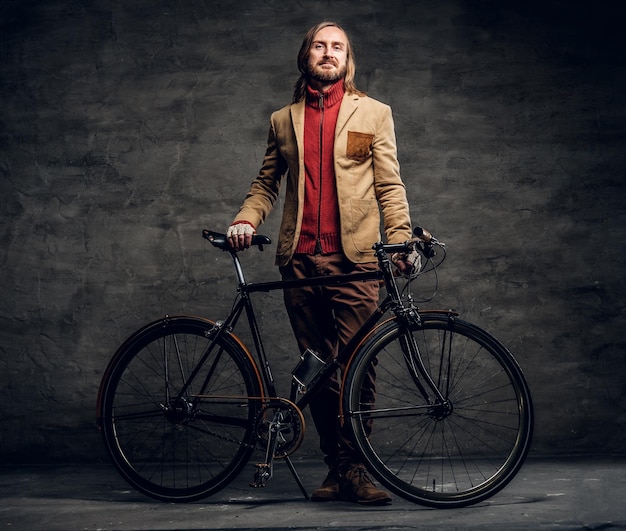 Moderner bärtiger Hipster im roten Pullover hält sein Fahrrad, während er für Fotografen posiert.