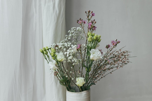 Moderner Blumenstrauß in Vase gegen Tüll und rustikale Wand Stilvolle Frühlingsblumen Eustoma Gypsophila und Chamelaucium Blumengrüße Platz für Text Fröhlicher Frauentag und Muttertag