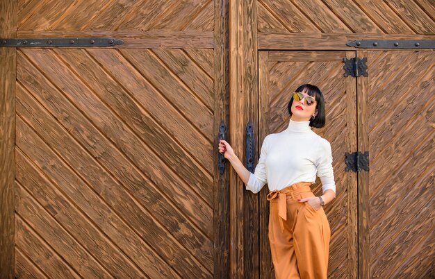 Moderner Brunette der Frau stehen im Freien hölzerner Hintergrund. Mädchen mit Make-up posiert in modischer Kleidung. Modisches Outfit schlanke große Dame. Mode- und Stilkonzept. Frauenspaziergang im eleganten Outfit.