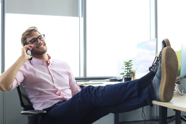 Moderner Geschäftsmann, der beim Sitzen im Büro am Telefon spricht.