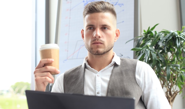 Moderner Geschäftsmann, der während der Mittagszeit Kaffee im Bürocafé trinkt und Laptop benutzt