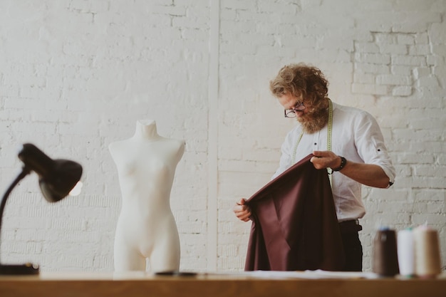 moderner junger Bekleidungsdesigner im Arbeitsprozess, ein Bekleidungsdesigner mit langen Haaren und Bart