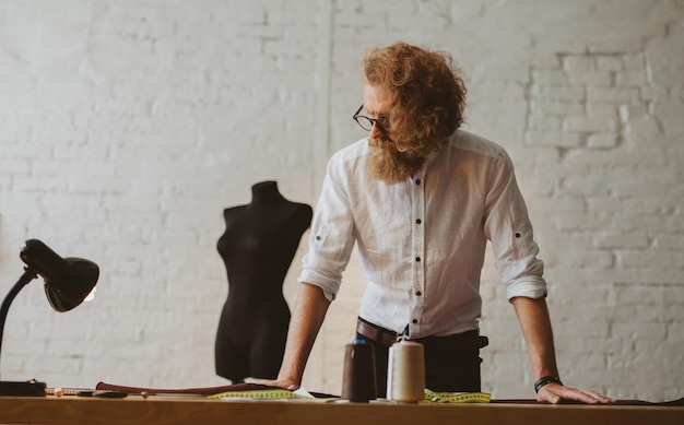 moderner junger Bekleidungsdesigner im Arbeitsprozess, ein Bekleidungsdesigner mit langen Haaren und Bart