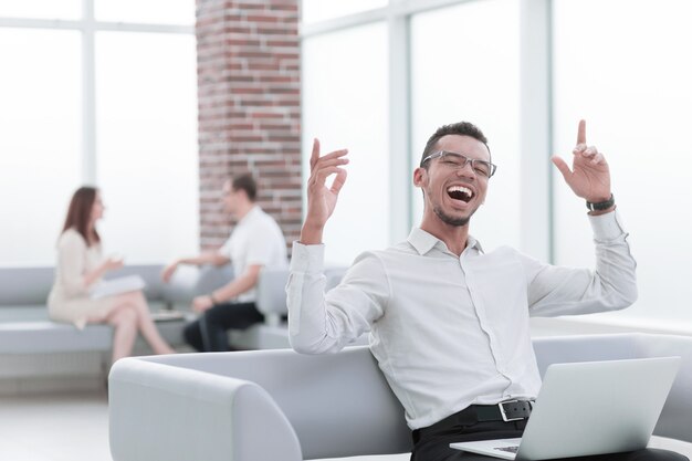 Moderner junger Mann mit Laptop, der auf Bürosofa sitzt. Menschen und Technologie