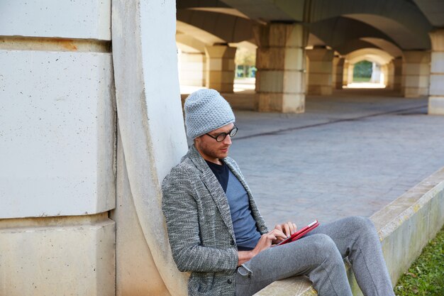 Moderner junger Mann mit Tablet-PC unter einer Brücke