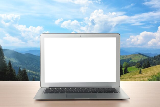 Moderner Laptop mit leerem Bildschirm auf dem Tisch und Blick auf die wunderschöne Berglandschaft