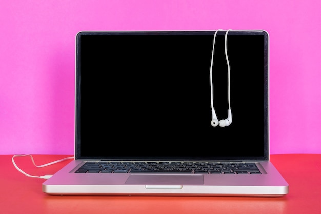 Moderner Laptop mit leerem Bildschirm und Kopfhörern auf buntem Hintergrund.