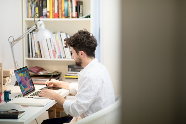 moderner Mann des hübschen Hippies, der nach Hause unter Verwendung des Laptops arbeitet