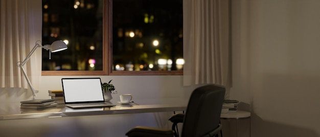 Moderner, minimalistischer Heimarbeitsplatz bei Nacht mit Laptop-Attrappe auf einem Tisch am Fenster