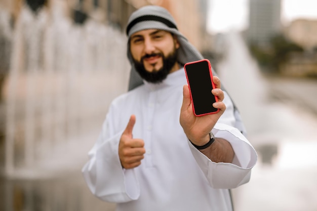 Moderner Naher Osten. Mann in Kaffiyeh und Thobe mit einem Telefon in der Hand