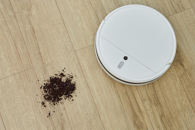 Foto moderner roboterstaubsauger, der schmutz oder erde vom holzboden entfernt smart-home-konzept