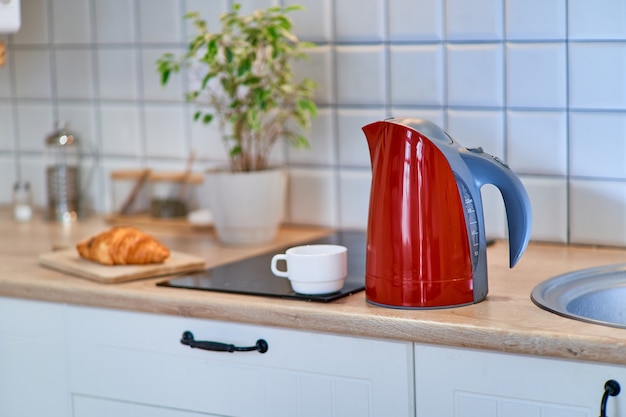 Moderner roter Wasserkocher mit einer cup weißen Tasse auf dem Tisch in der Küche zu Hause