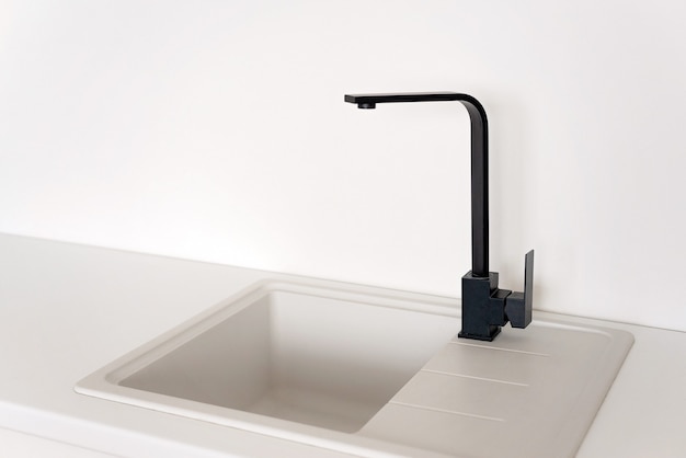 Moderner schwarzer Wasserhahn in einem weißen Küchenspülbecken. Weicher selektiver Fokus.