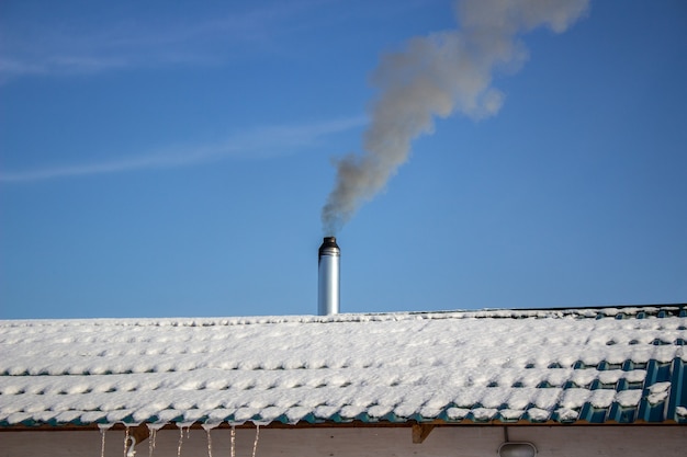 Moderner Stahlschornstein einer russischen Sauna mit Schnee bedeckt vor blauem Himmel.