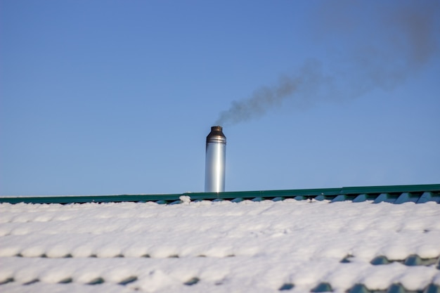 Moderner Stahlschornstein einer russischen Sauna mit Schnee bedeckt vor blauem Himmel.