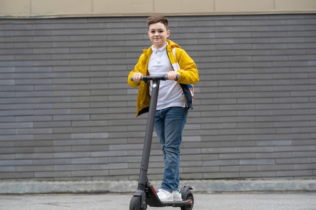 Moderner Teenager reitet auf Elektroroller auf Backsteinmauerhintergrund.