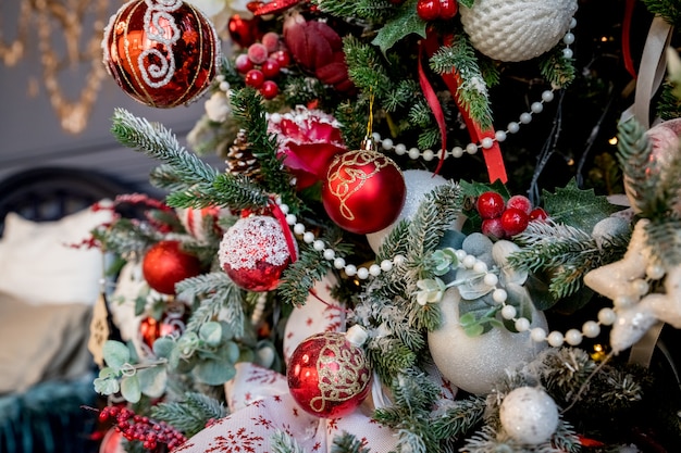 Moderner Weihnachtsbaum, verziert mit Weinleseverzierungen, ratan Bällen, Leinwand- und Schottenstoffbändern, hölzernen Schneeflocken, roten Beeren und Bällen, roten weißen Bällen Weihnachtsflitter.