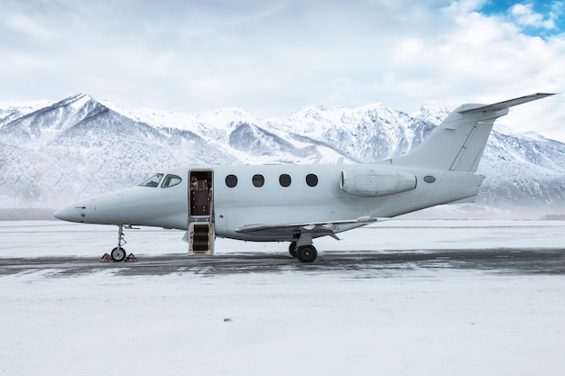Moderner weißer Business-Jet mit geöffneter Gangway-Tür auf dem Hintergrund hoher schneebedeckter Berge