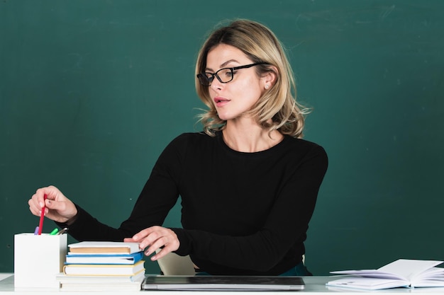 Modernes attraktives Lehrerporträt einer intelligenten jungen Frau mit Brille mit Buch an der Tafel in cl