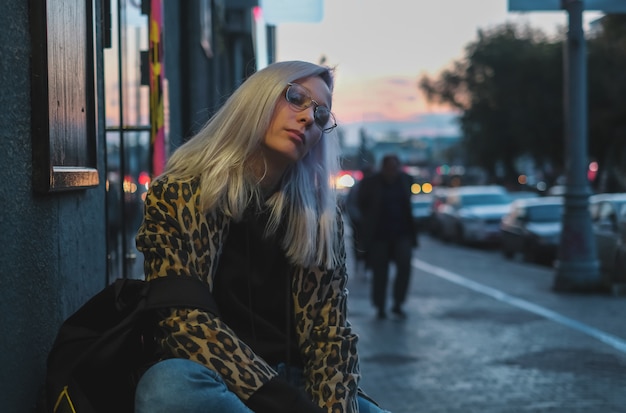 Modernes blondes Mädchen mit Gläsern im Leopardmantel an Straße I