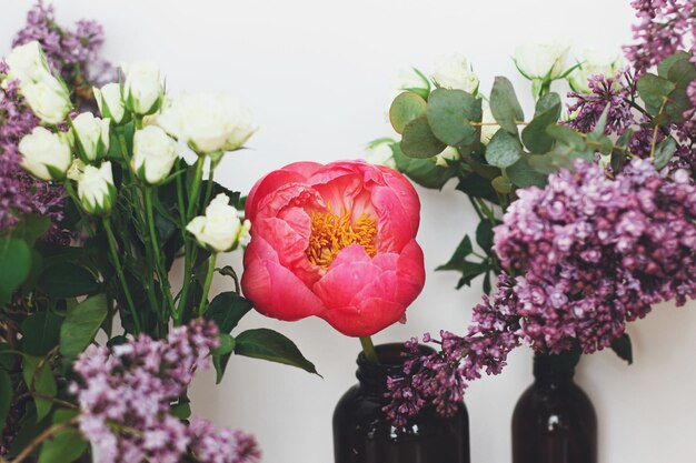 Modernes Blumenstillleben Schöne Pfingstrose lila Rosen Blumen und Eukalyptus in Glasflaschen