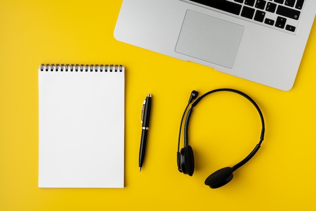 Foto modernes büro-desktop mit leerem notizblock-stift-headset und laptop auf gelbem hintergrund