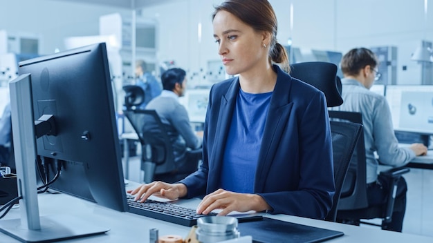 Modernes Fabrikbüro Porträt einer jungen und selbstbewussten weiblichen Industrieingenieurin, die an einer Computerfabrik mit Industrie-Design-Ingenieuren arbeitet, die an Computern arbeitet CNC-Maschinenwerkstatt