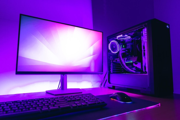 Modernes Gaming-Computer-Setup mit Display-Wasserkühlung, Gehäuse, Tastatur, Maus auf Gaming-Matte Lila LED-Licht im Hintergrund